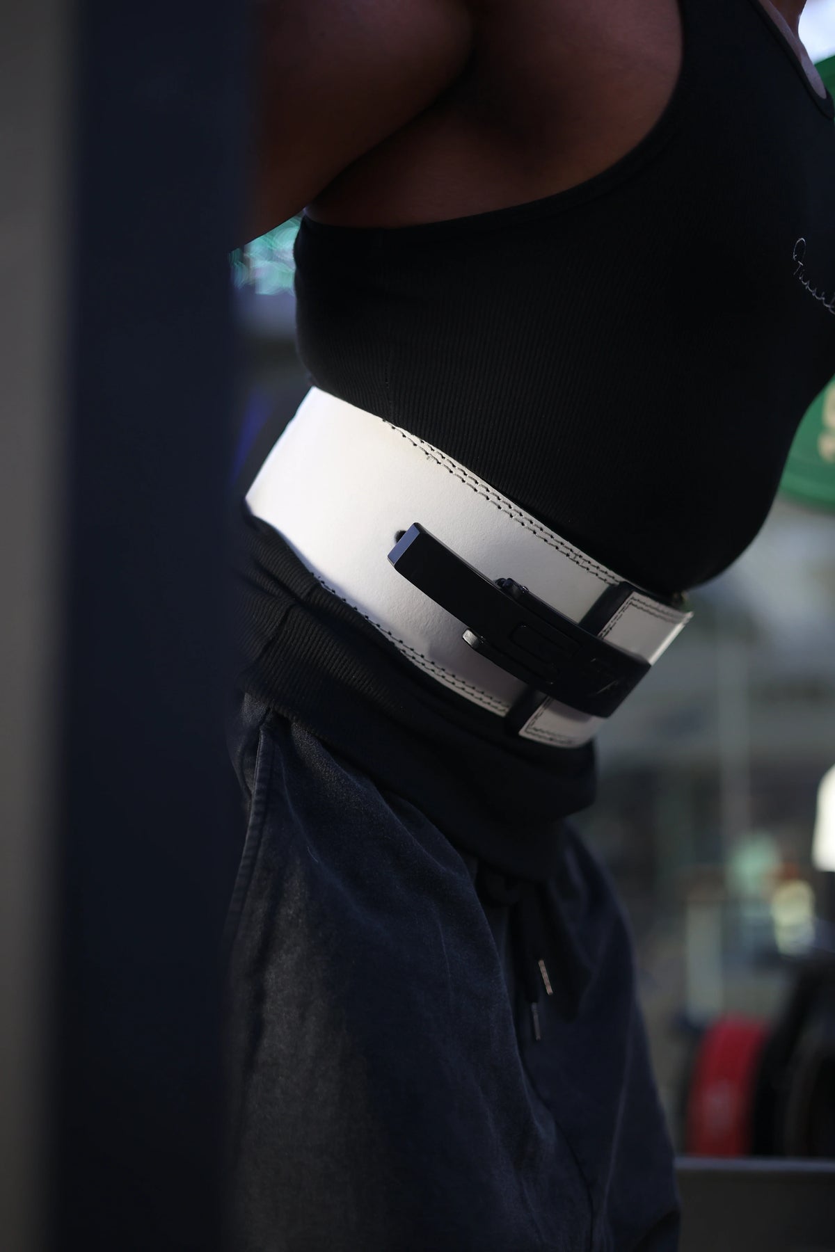 A person wearing a white leather powerlifting belt with a black lever buckle around their waist.